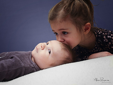 Photo d'une enfant embrassant le front de son petit frère.